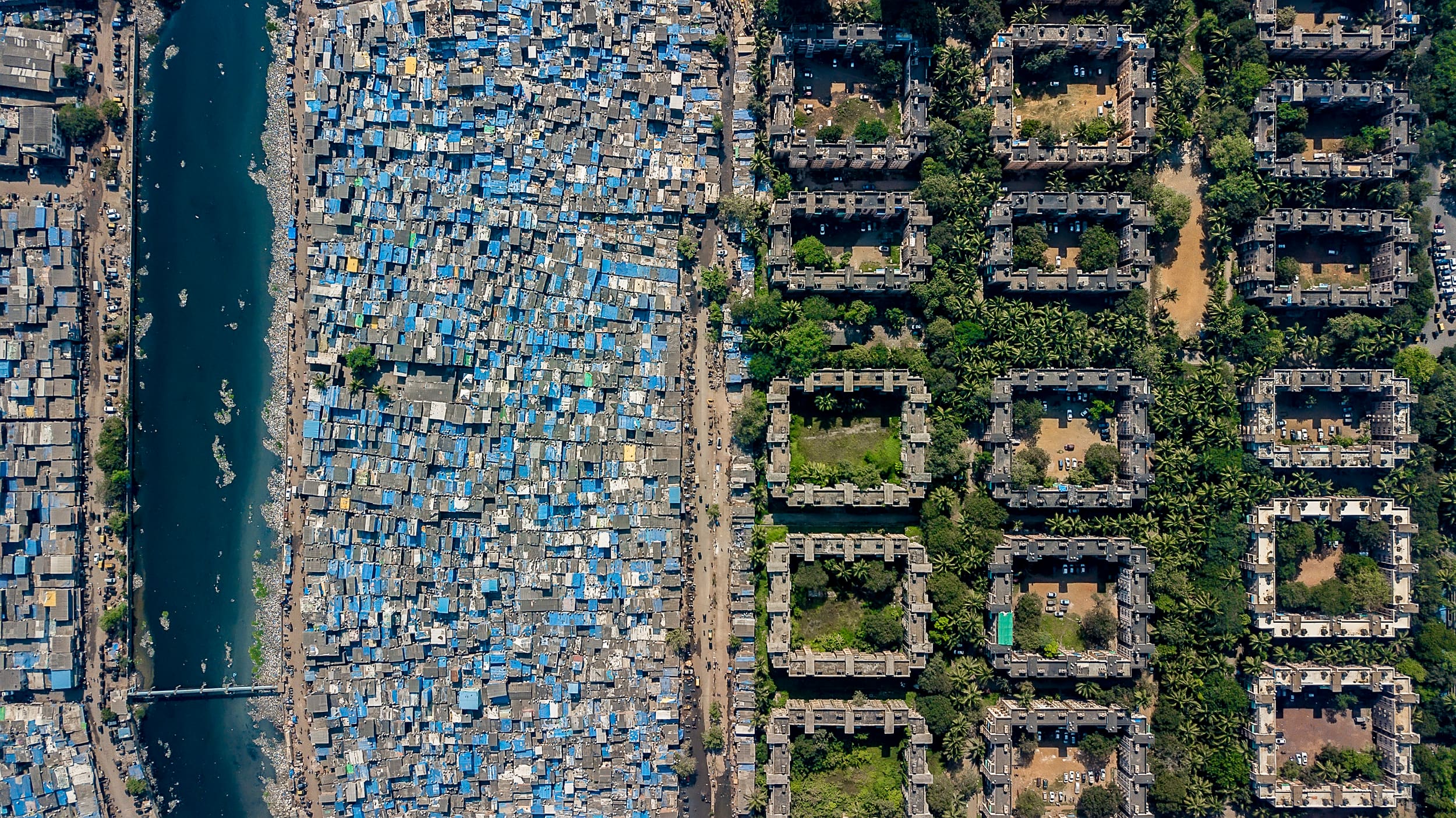 A creek, a dense settlement, a road, and apartment blocks beyond, in Mumbai from the air