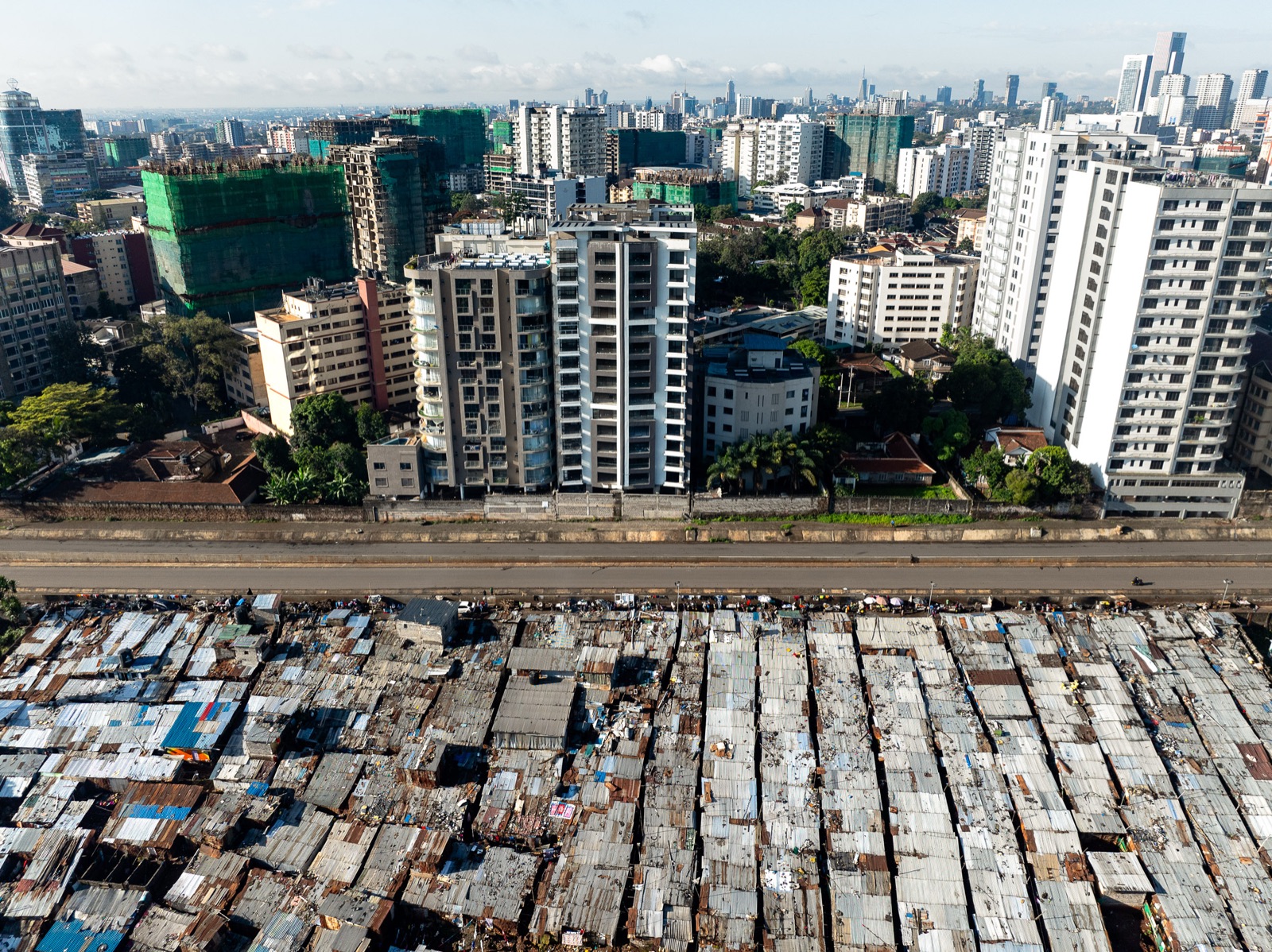 Nairobi from the air: rows of iron roofs in the Deep Sea settlement fill the foreground, a road separates them from new apartment towers, and the city centre stands on the horizon